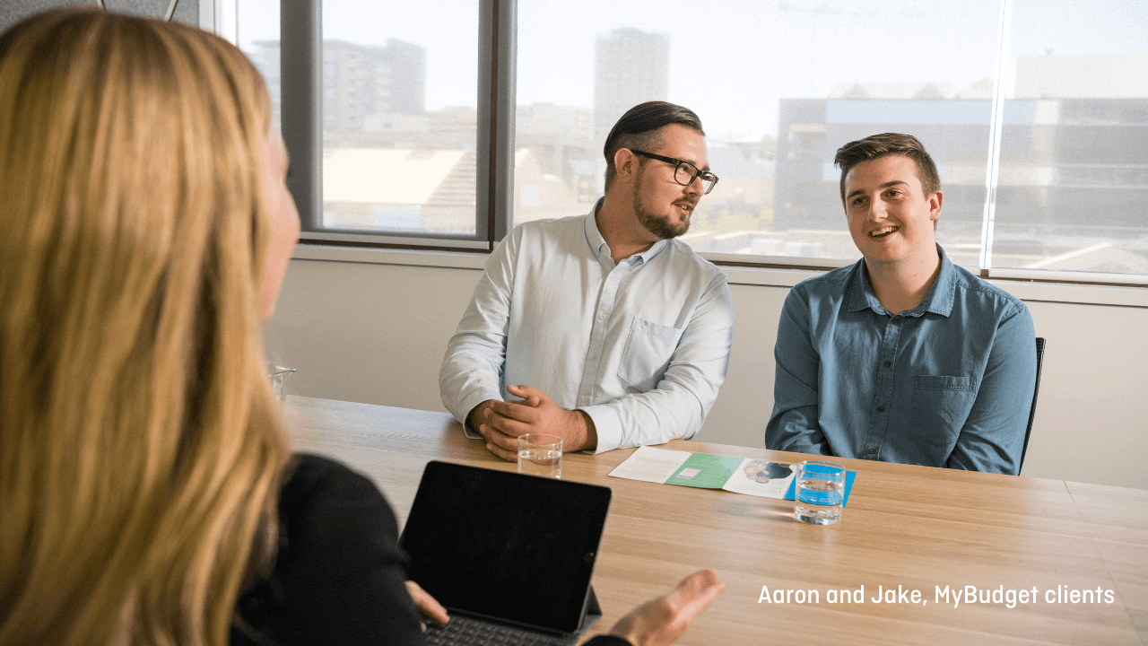 Two men sitting at a table chatting with a MyBudget Money Coach agent on the other side of the table.