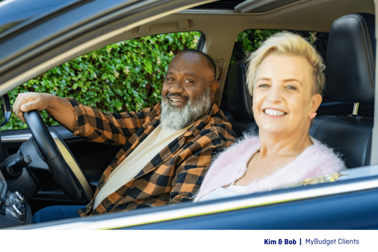 Kim and Bob, MyBudget clients, smiling in their car after reducing debt and taking control of their finances.