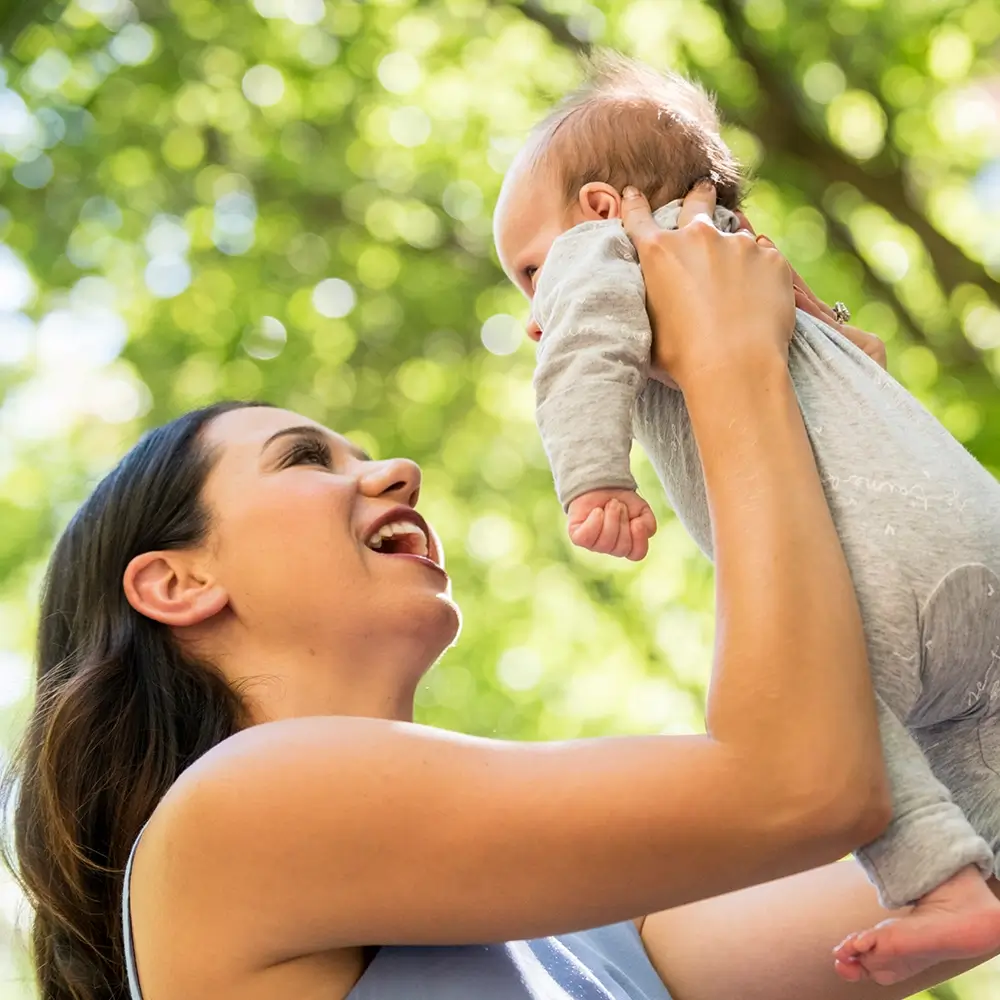 MyBudget client Jaz holding her newborn outdoors, representing New Zealand parents preparing and budgeting for a new baby.